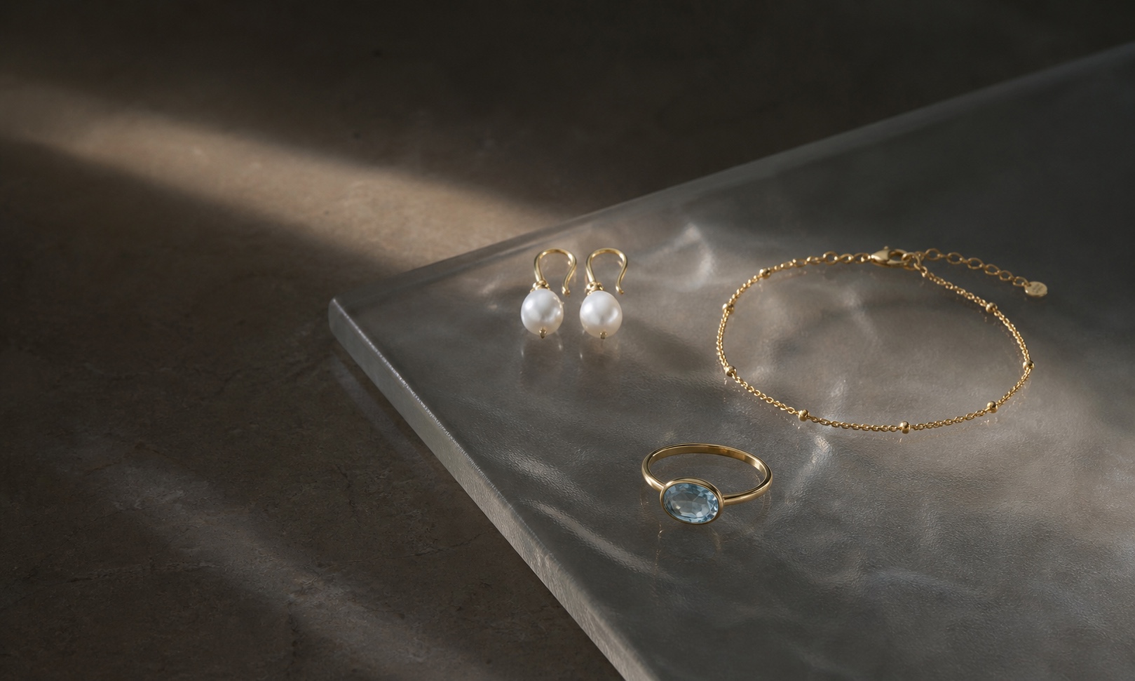 Pearls, pale blue gemstone ring, and fine gold bracelet held in a narrow beam of light