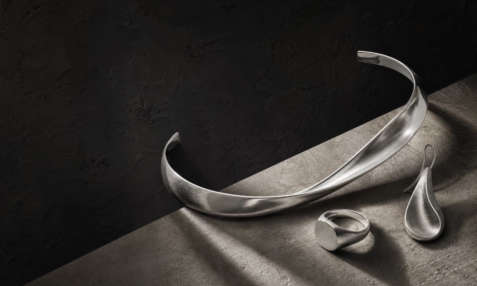 Sculptural silver collar, signet, and drop earrings casting architectural shadows